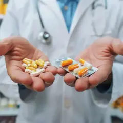 Farmaceuta w białym fartuchu trzyma w dłoniach tabletki i kapsułki w blistrze.