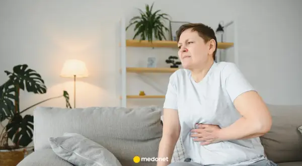 Kobieta z bólem brzucha, być może potrzebuje metoclopramidum polpharma. Siedzi na kanapie w salonie.