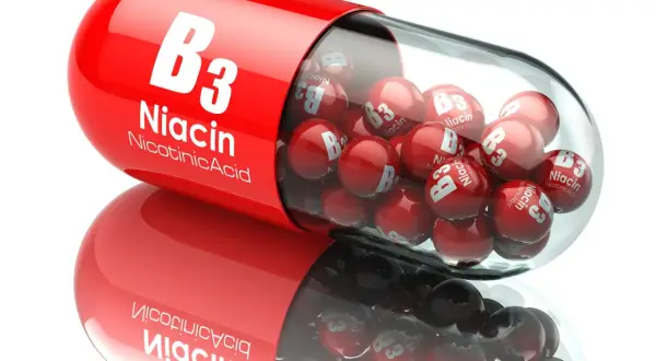 Czerwona kapsułka wypełniona małymi, błyszczącymi kulkami z napisem "B3 Niacin Nicotinic Acid". To witamina PP w pigułce.