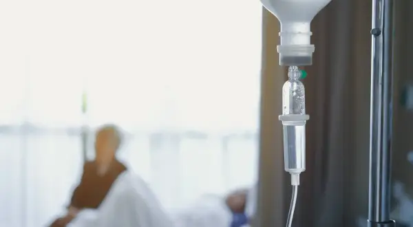 Kroplówka dożylna, symbol nadziei i walki z chorobą. W tle niewyraźna postać pacjenta, który przechodzi chemioterapię.
