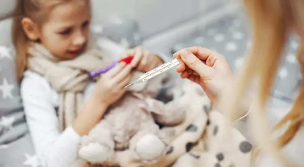 Dziecko z gorączką, objawy rotawirusa. Mama mierzy temperaturę termometrem.