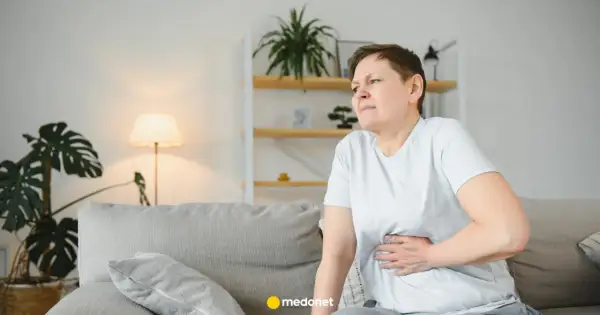 Kobieta z bólem brzucha, być może potrzebuje metoclopramidum polpharma. Siedzi na kanapie w salonie.